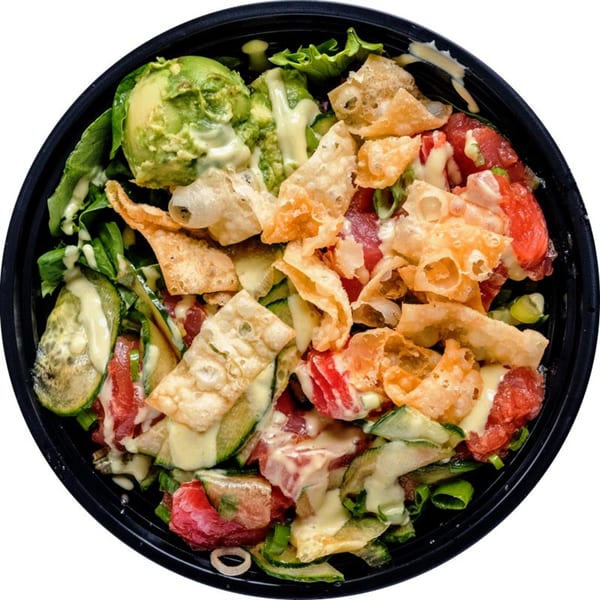 Overhead view of a colorful salad with avocado, red tomatoes, green vegetables, and crispy wontons.