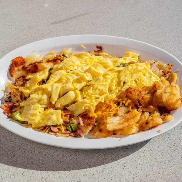 A Joe's New York Diner breakfast skillet with scrambled eggs, home fries, bacon, and cheese.