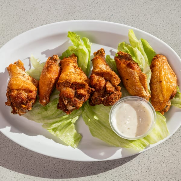 Six crispy fried chicken wings on a bed of lettuce with a side of ranch dressing.