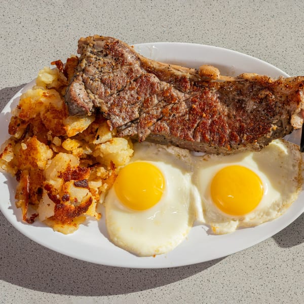Joe's New York Diner's steak and eggs breakfast with crispy hash browns on a white plate.
